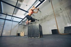 Junge, blonde, trainierte Frau mit rosa Sport Top und schwarzer leggins springt auf eine schwarze Kiste