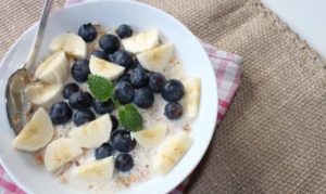 Keramikschüssel gefüllt mit Bananenstückchen, Blaubeeren und Molke, dazu etwas Minze