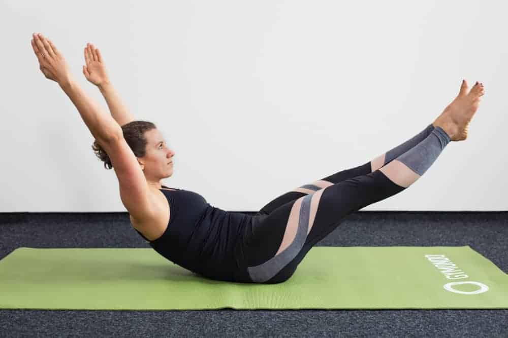 Junge Frau in Rückenlage mit angehobenen Beinen auf einer hellgrünen Trainingsmatte macht Pilates Double Leg Stretch