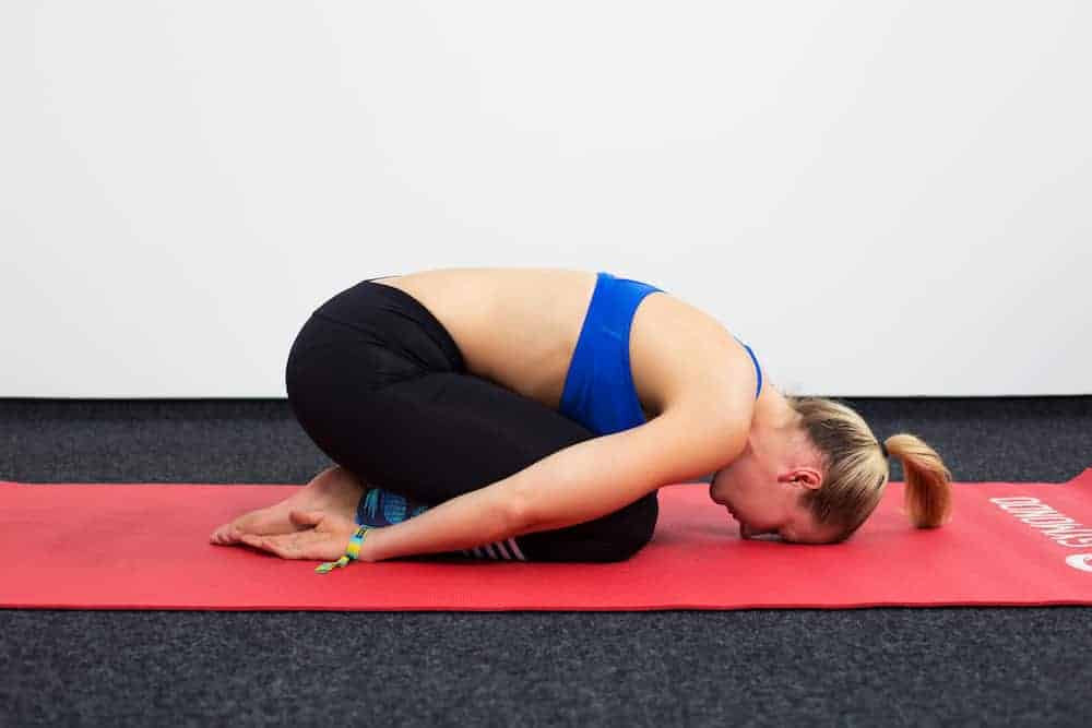 Junge Frau auf einer roten Trainingsmatte macht das Kind, die Haltung des Kindes aus dem Yoga