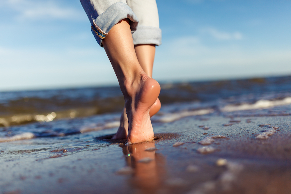 Frau läuft am Strand barfuß durch den Sand, denn barfußlaufen ist gesund