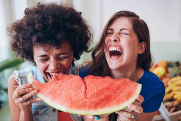 Zwei junge Frauen lachen und essen zusammen ein großes Stück Wassermelone