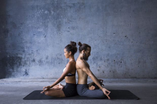 Frau und Mann sitzen Rücken an Rücken und machen Yoga