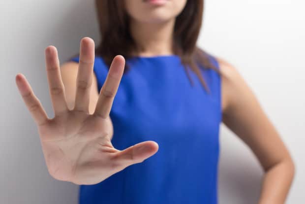 Frau in blauem Kleid streckt die Hand nach vorne und sagt Nein