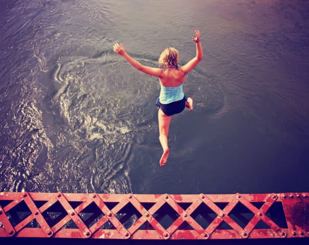 Junge Frau springt aus großer Höhe ins Wasser