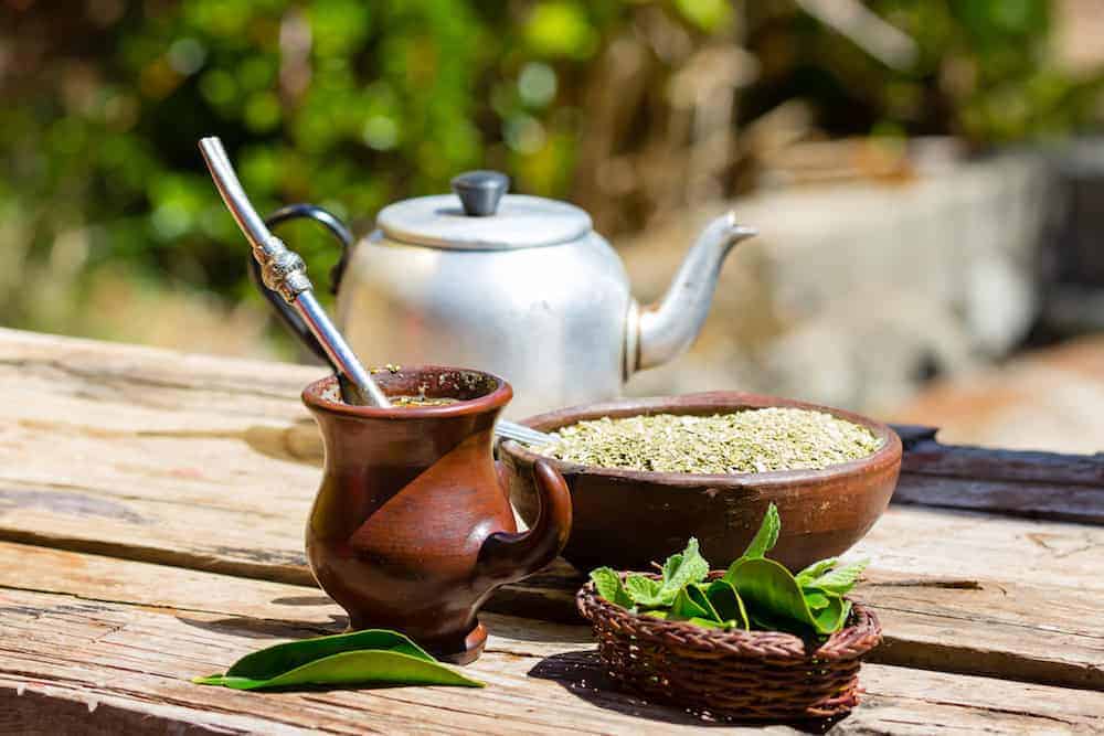 Teekanne mit Mate Tee auf Holztisch, braune Mate Tee Tasse und Schale mit Mate Tee Pulver