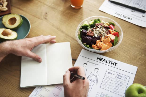 Ein Notizbuch mit Aufzeichnungen zu einer geusnden Ernährung auf einem Tisch mit gesundem Essen