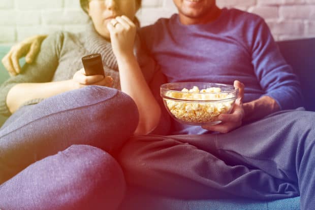 einPaar sitzt auf dem Sofa und isst poppcorn und  trinkt bier