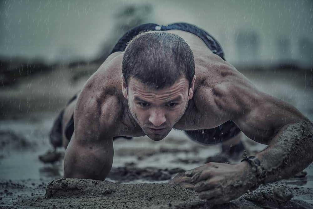 Durchtrainierter Mann macht Crawling Fitness und krabbelt durch den Schlamm