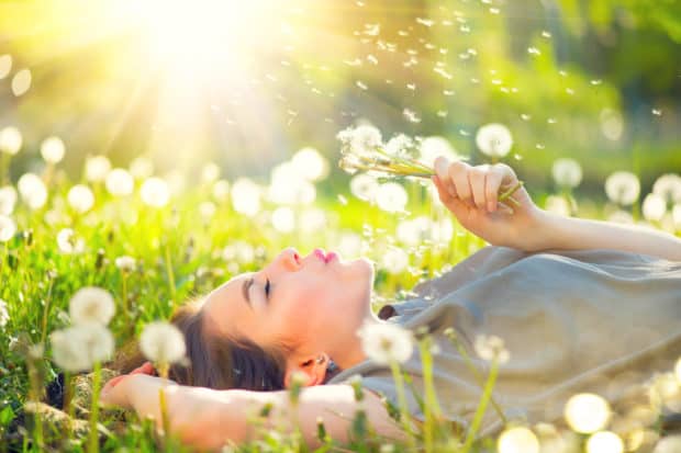 Junge Frau genießt den Moment liegt auf einer Wiese und pustet gegen eine Pusteblume.