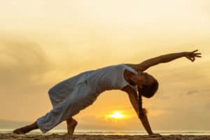 Frau macht Yoga am Meer auf Bali im Sonnenuntergang