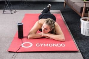 Frau in Sportkleidung liegt auf roter Trainingsmatte und ruht sich aus nach dem Workout mit dem GYMONDO Alexa Skill